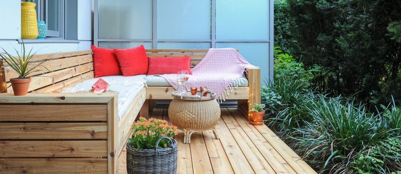 A cedar decking with a comfortable sitting area with a small table with glasses on it and plants
