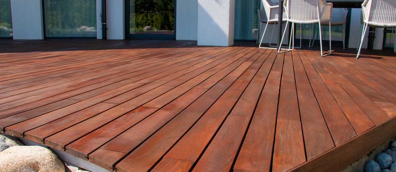 A wooden deck on a gravel garden with furniture installed with patio and deck installation service.