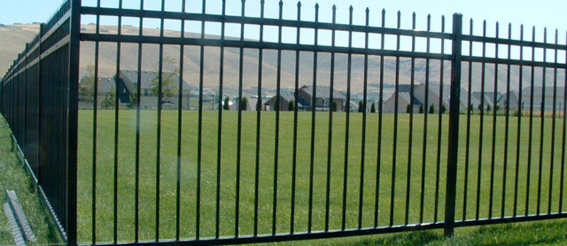 An ornamental iron fence surrounds a remote residential complex with lots of open space around it.