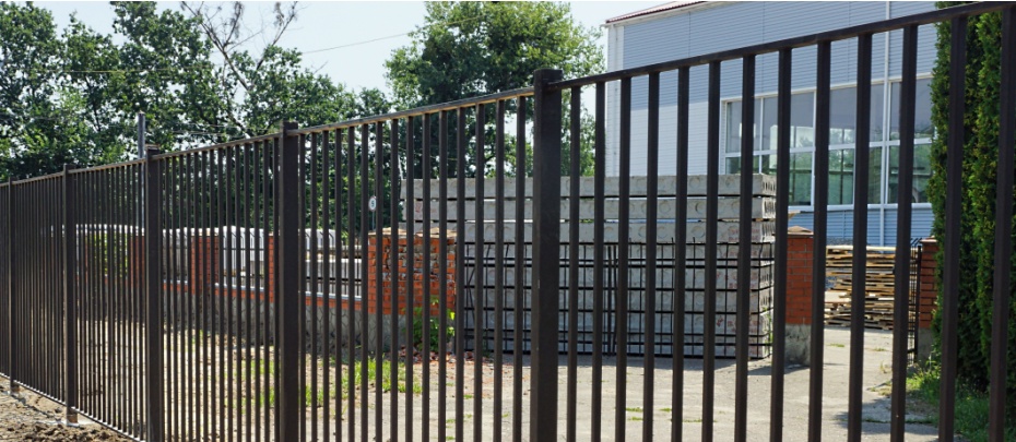 An ornamental iron fence surrounds a remote residential complex with lots of open space around it.
